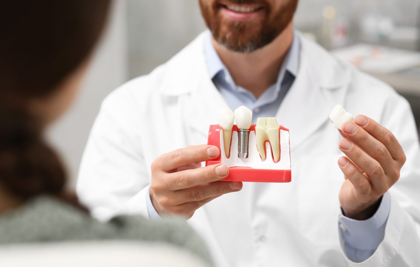 Doctor with educational model of dental implant consulting patient in clinic, closeup