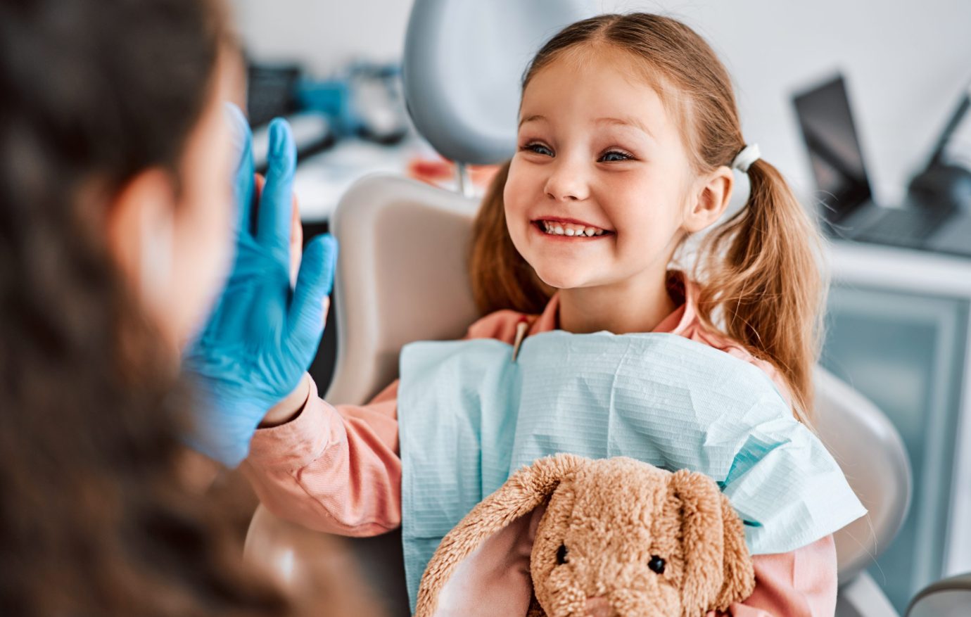 At the doctor's appointment. A candid emotional photo of a child sitting in a dental chair, holding a toy rabbit and cheerfully giving a high-five to the nurse.