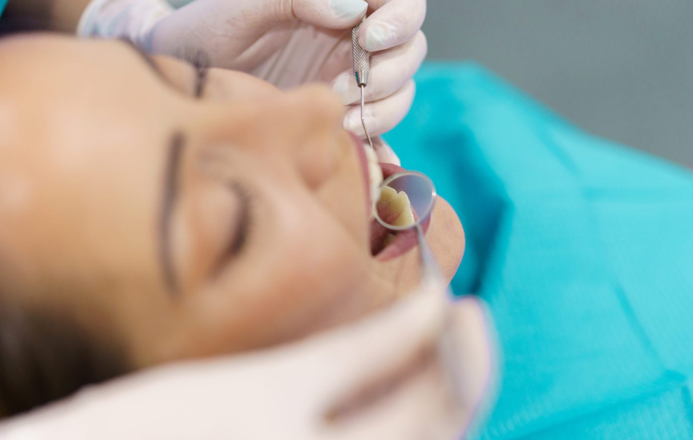 Dentist checking the inside of her female patient's teeth with a dental mirror.